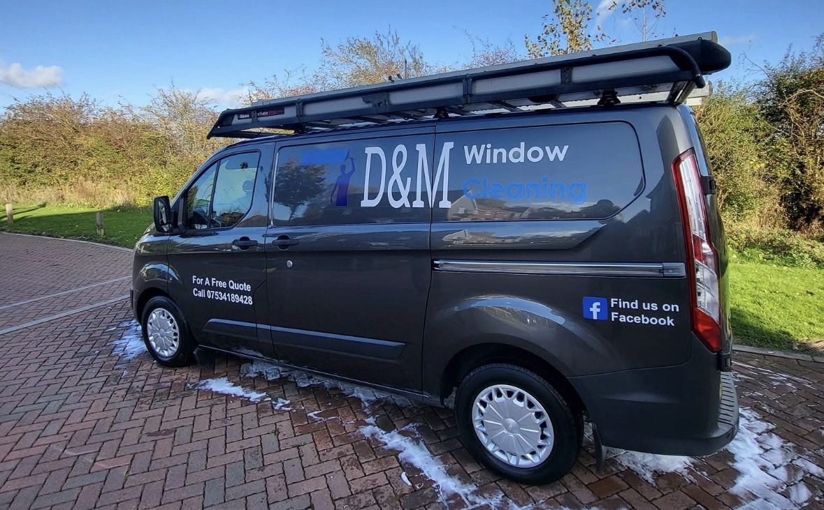 The dark grey D&M Window Cleaning van with a ladder rack, lettered For A Free Quote Call 07534189428