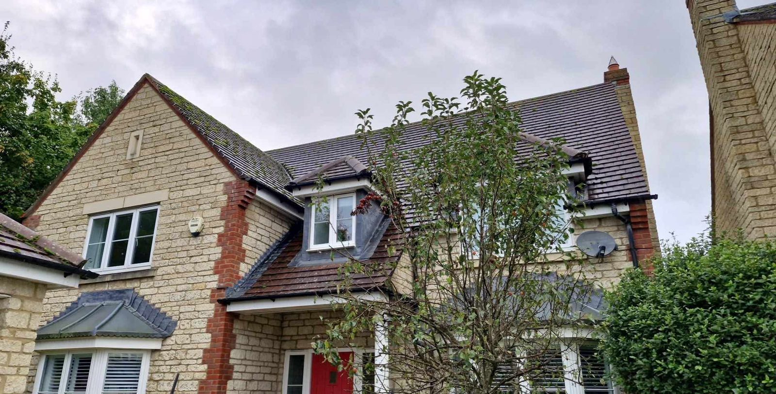 A large Cotswold stone detached house with dormer windows and a tree in front
