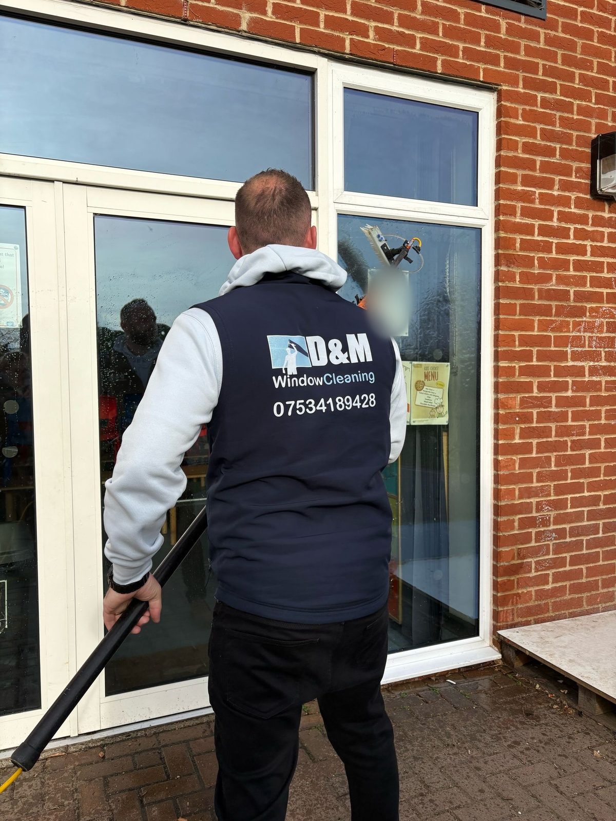 Matthew from behind in a navy D&M Window Cleaning gilet, cleaning a door with a water-fed pole brush